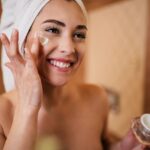 Lächelnde Frau trägt Feuchtigkeitscreme auf – Vorbereitung auf eine Hydrafacial Behandlung für ein strahlendes Hautbild